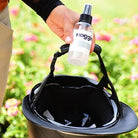 Person holding a spray bottle over a riding helmet in a garden setting