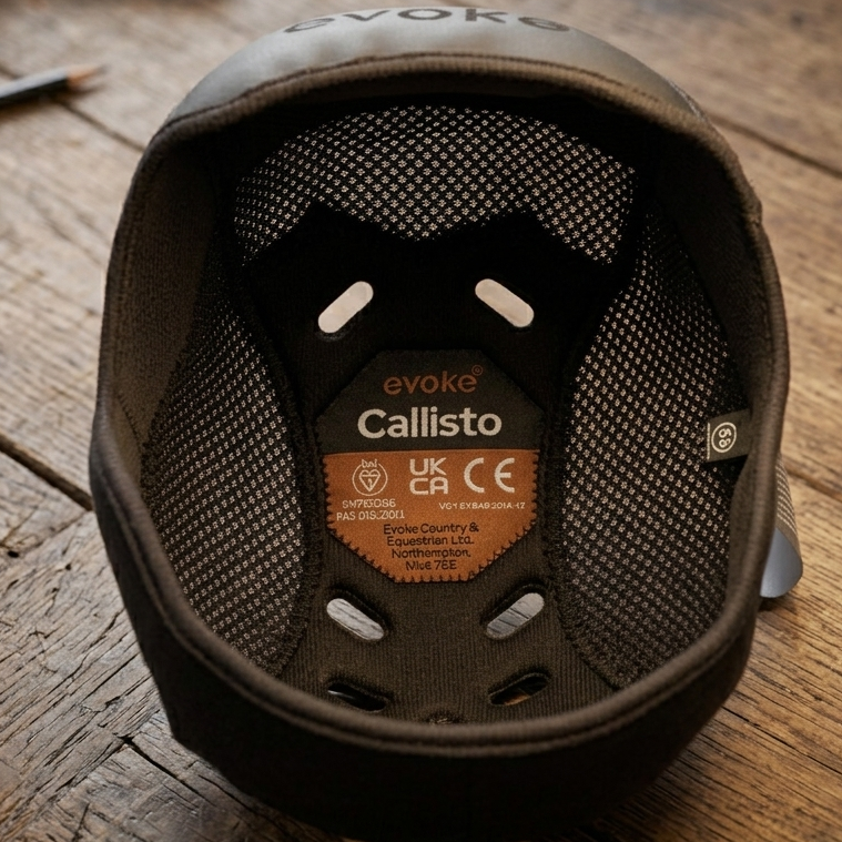 The interior of a dark gray or black riding helmet, showing the Callisto liner and the brand label, resting on a rustic wooden workbench with tools in the background.