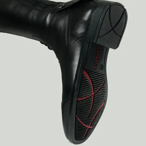 Close-up of a black leather boot with a brand label on a light gray background