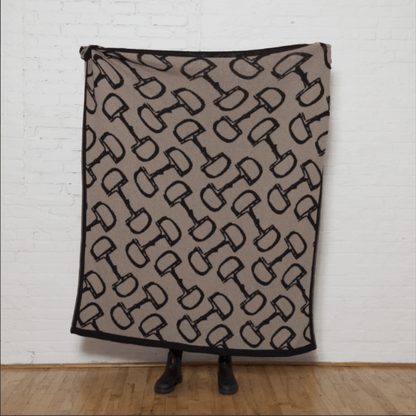 In2Green - Eco Bits Reversible Throw held by a model in front of a white wall and wood floor. The throw is hemp with black snaffle bits and a black border.
