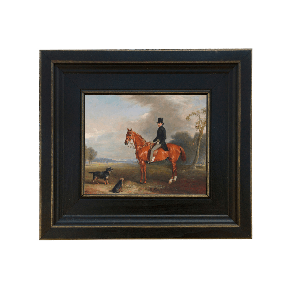 Black framed print of a man riding a horse in hunt gear with hounds